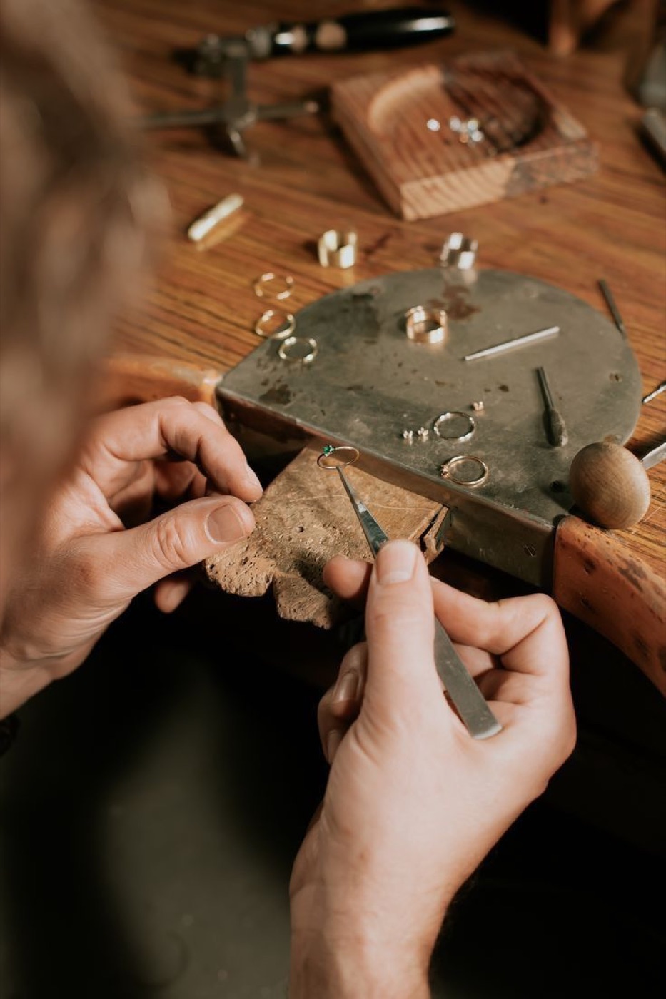 A setter tensioning the six claws of a diamond solitaire by hand under magnification